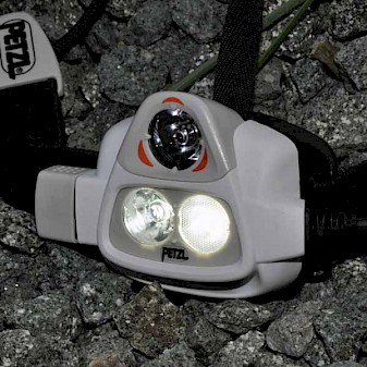 Close up image of the Petzl Nao 575L showing the light sensor at the top and the two lamps below. to the left of the picture the control dial can be seen.