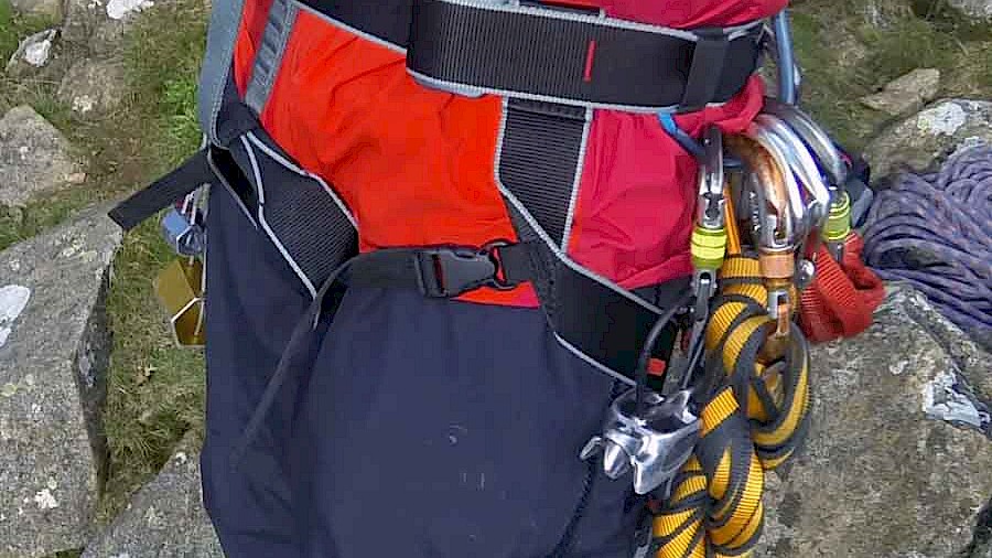 Side-on image showing the DMM Super Couloir being worn, clearly showing the quick release leg buckles, double back buckle waist closure and the simple waist attachment through the belay loop.
