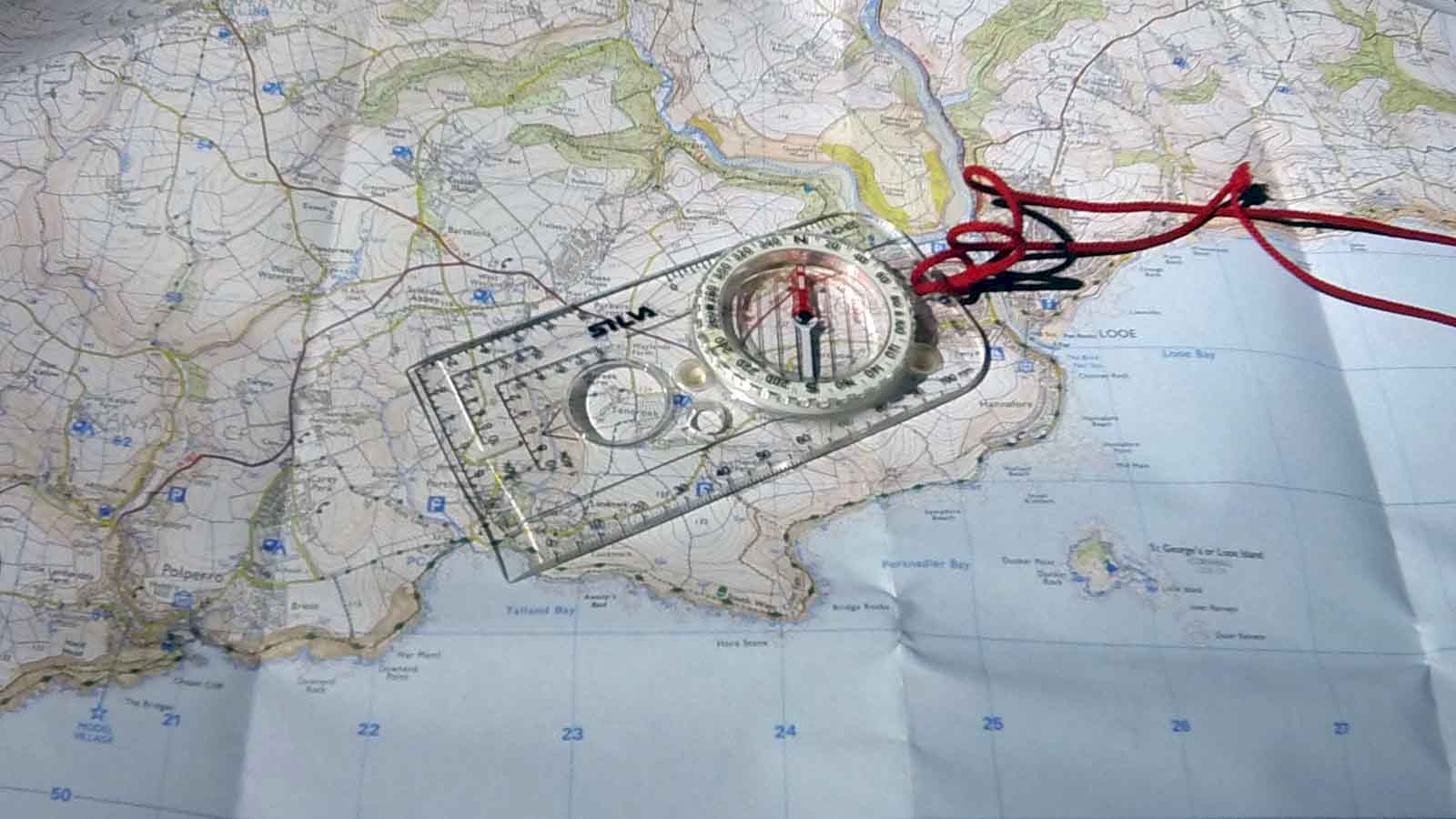 A Silva compass on top of a 1:25,000 OS Explorer map of South East Cornwall, aligned in West South Westerly direction along the measured nautical mile between Looe and Polperro.